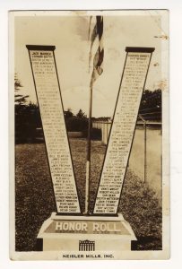 A V-shaped honor roll monument with the names of servicemembers written on it. An American flag flies in the middle on the monument.