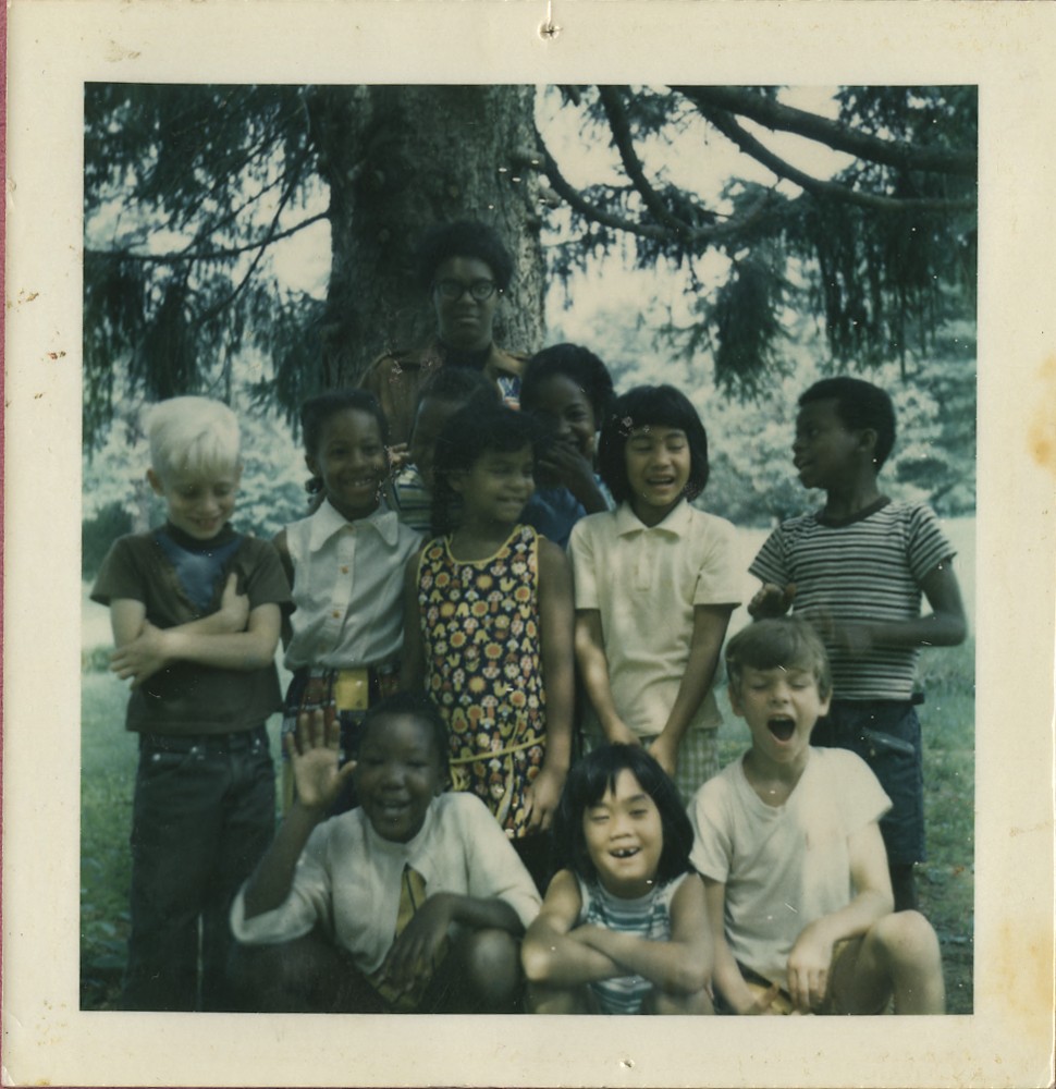 Group of children smiling at the camera in front of a pine tree