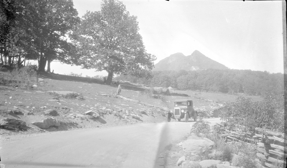 Ford Model T driving on a road with Grandfather Mountain in the background, black and white photograph