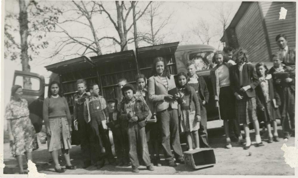 A group of students and teachers from Goins School, a Native American school, stand in front of a visiting bookmobile.