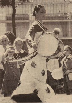 A young woman in cultural garb banging on a drum.