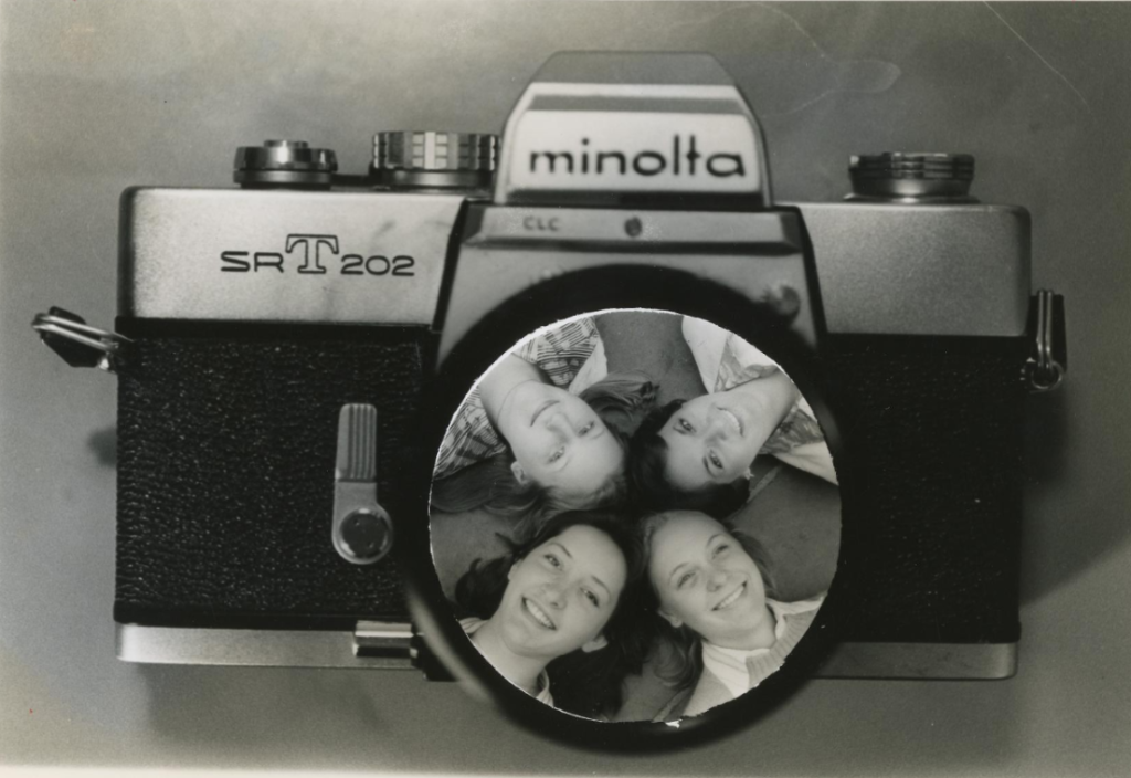A circular cutout image of four people laying on the ground with their heads touching is pasted onto the lens area in a picture of camera.