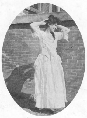 A black-and-white photograph of a young woman in front of a brick wall. 