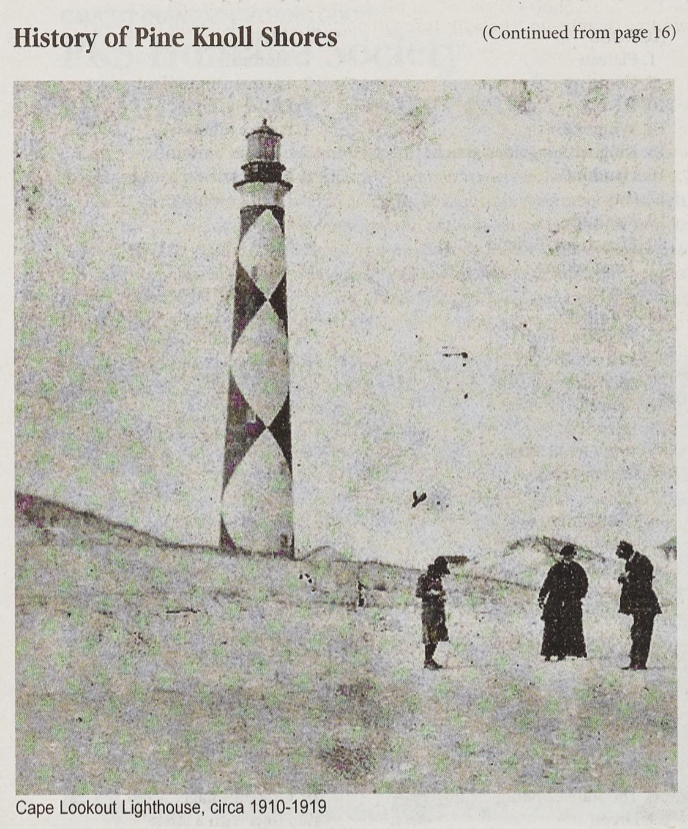An black-and-white photograph from the 1910s featuring Cape Lookout Lighthouse. Three people stand on the beach in the lefthand corner of the photograph. Behind the party, dunes and the large lighthouse take up the left side of the image.