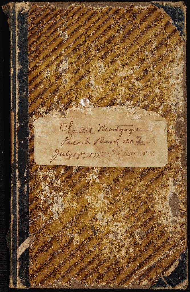 The front cover of the chattel mortgage book. Written in brown on the book's front label is "Chattel Mortgage Record Book No. 2. July 17th, 1877 to Feb 22nd, 1899". The rest of the cover features a golden brown marbled pattern that is worn and flaked in some areas.