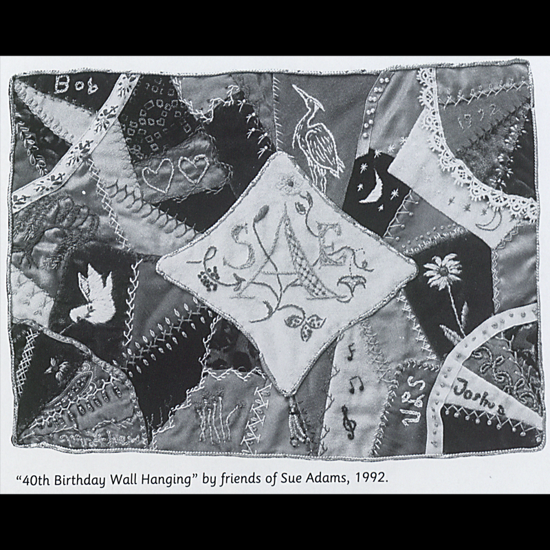 Quilt made in the crazy quilt style; it has many small pieces of fabric (most solid colors) sticked together with a large diamond shape white piece of fabric in the middle. Inside the diamond is this stitched initials of the recipient ‘SAE’ and small floral accents added around the initials; throughout the quilt there are the names of contributors stitched into the quilt as well. There are many visible embellished stitches on top of the regular stitches, as well as lace and embroidered/stitched designs like flowers, moon, stars, dove, crane, hearts, music notes, and a butterfly.