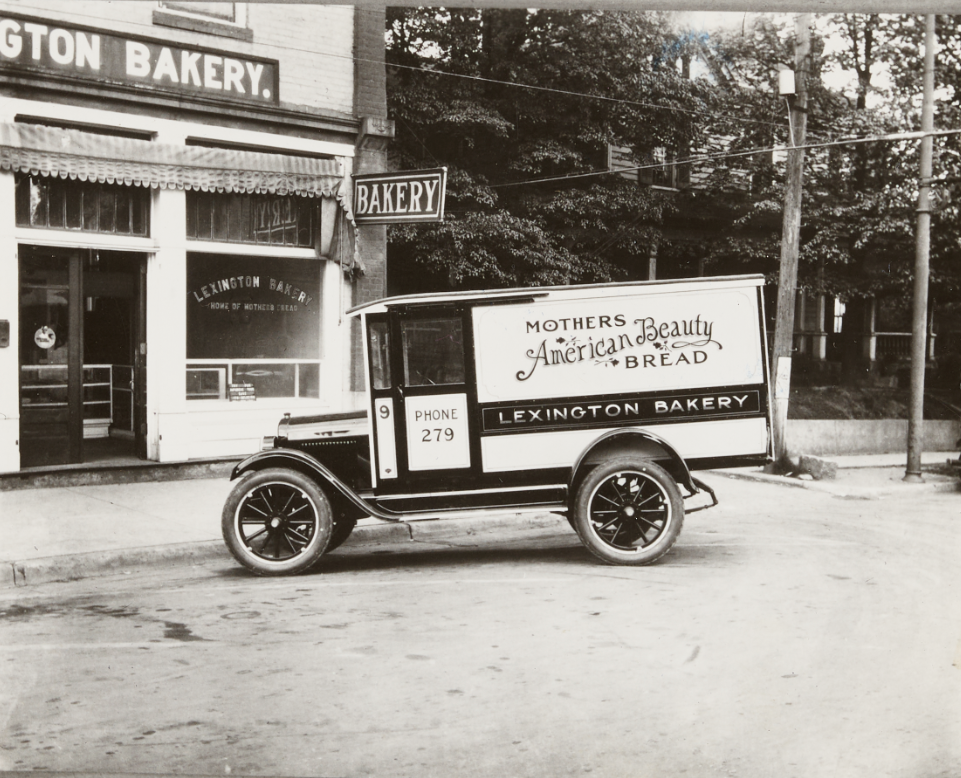 A 1920s delivery car used by Lexington Bakery and shown parked in front of the bakery. The car has the text "Mother's American Beauty Bread," "Lexington Bakery," and "Phone 279" printed on its rectangular body.
