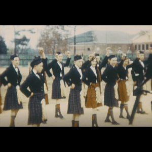 Over a dozen young dancers in kilts and traditional Scottish attire getting prepared to perform a Scottish dance. They are raising their left hands and extending their right feet to begin the performance.