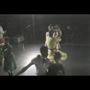 A color photo that shows two couples dancing, one pair in the middle of a slight dip and the other having one person spinning the other. They are on a dance floor and other people are seen to the side about to start dancing on the dance floor.