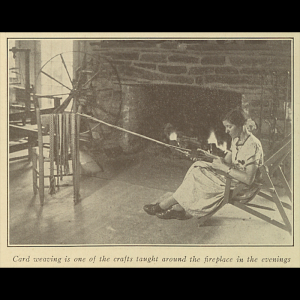 A person sits by a fireplace in a dress while using a loom to weave cord.