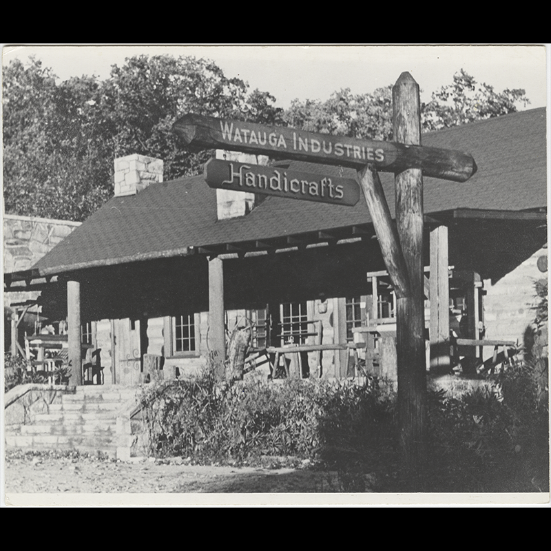 Stone cabin-style building in the background with a signpost in the foreground that reads “Watauga Industries Handicrafts.”