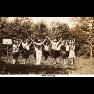 Sepia photograph of a group of young people folk dancing, arranged in a circle and holding hands raised high.