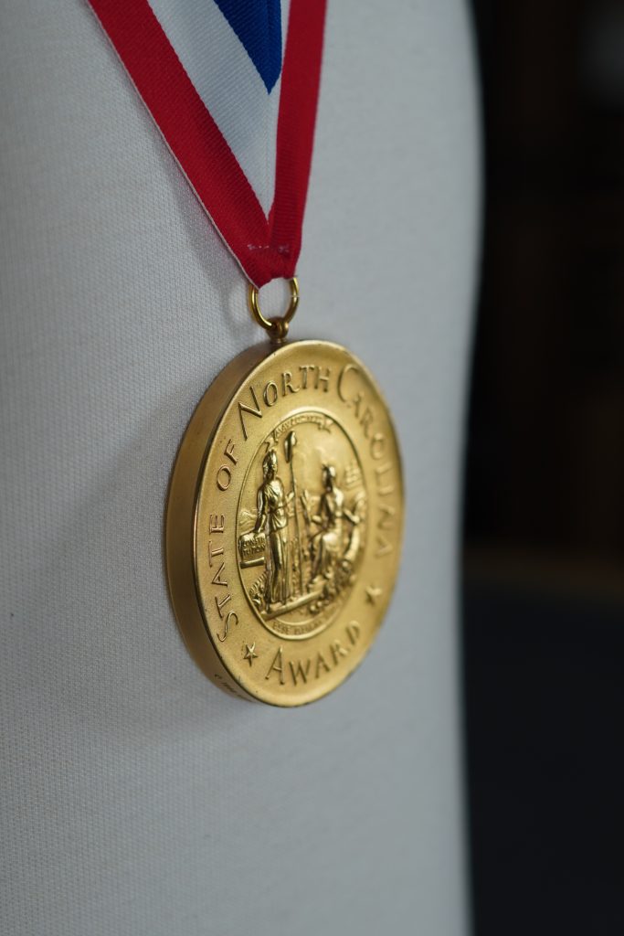 Closeup of a gold medal that says "State Of North Carolina Award" on it with the state crest