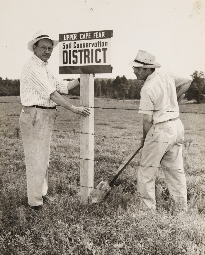 Two unidentified adults installing a sign for the Upper Cape Fear Soil Conservation District.