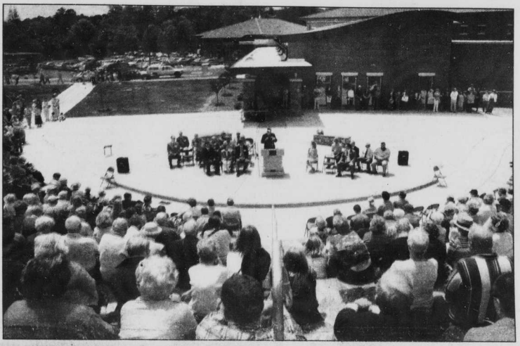 Image from the Transylvania Times showing hundreds of people sitting in an amphitheater listening to a speaker in the center of the image.