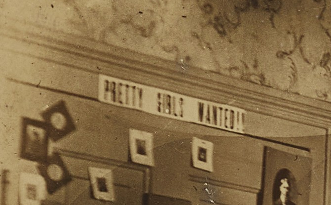 Close up of the door featured in a 1903 picture of a dorm room at the University of North Carolina at Chapel Hill. Along the top of the door a white horizontal sign reads "Pretty Girls Wanted!!"