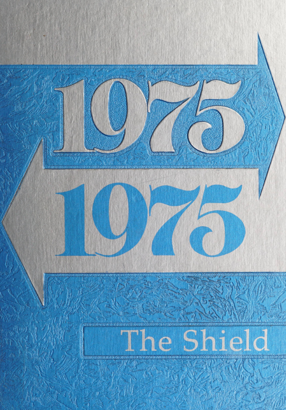 The cover of the Vaiden Whitley High Shool yearbook for the year 1975. The yearbook cover is half silver and half sky blue. It features two large horizontal arrows pointing in opposite directions across the page. The top arrow is sky blue and contains "1975" written in large silver text, while the bottom arrow is silver and contains "1975" written in sky blue text. Towards the bottom right of the cover is a sky blue banner that has the title "The Shield" written in silver.
