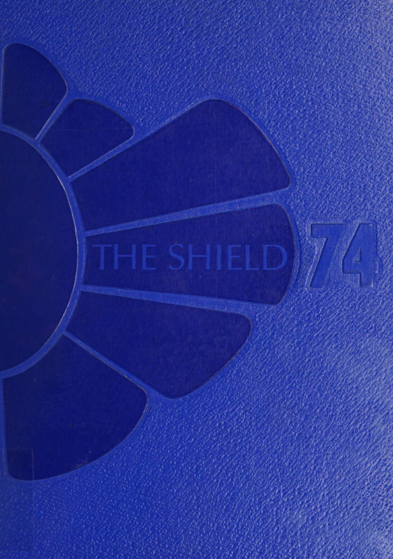 The cover of the Vaiden Whitley High Shool yearbook for the year 1974. The royal blue yearbook features half of an abstract flower-like design on the left side of the cover that is dark blue. The title "THE SHIELD" is printed in royal blue on a petal from the flower-like motif. "74" is embossed on the right side of the cover.